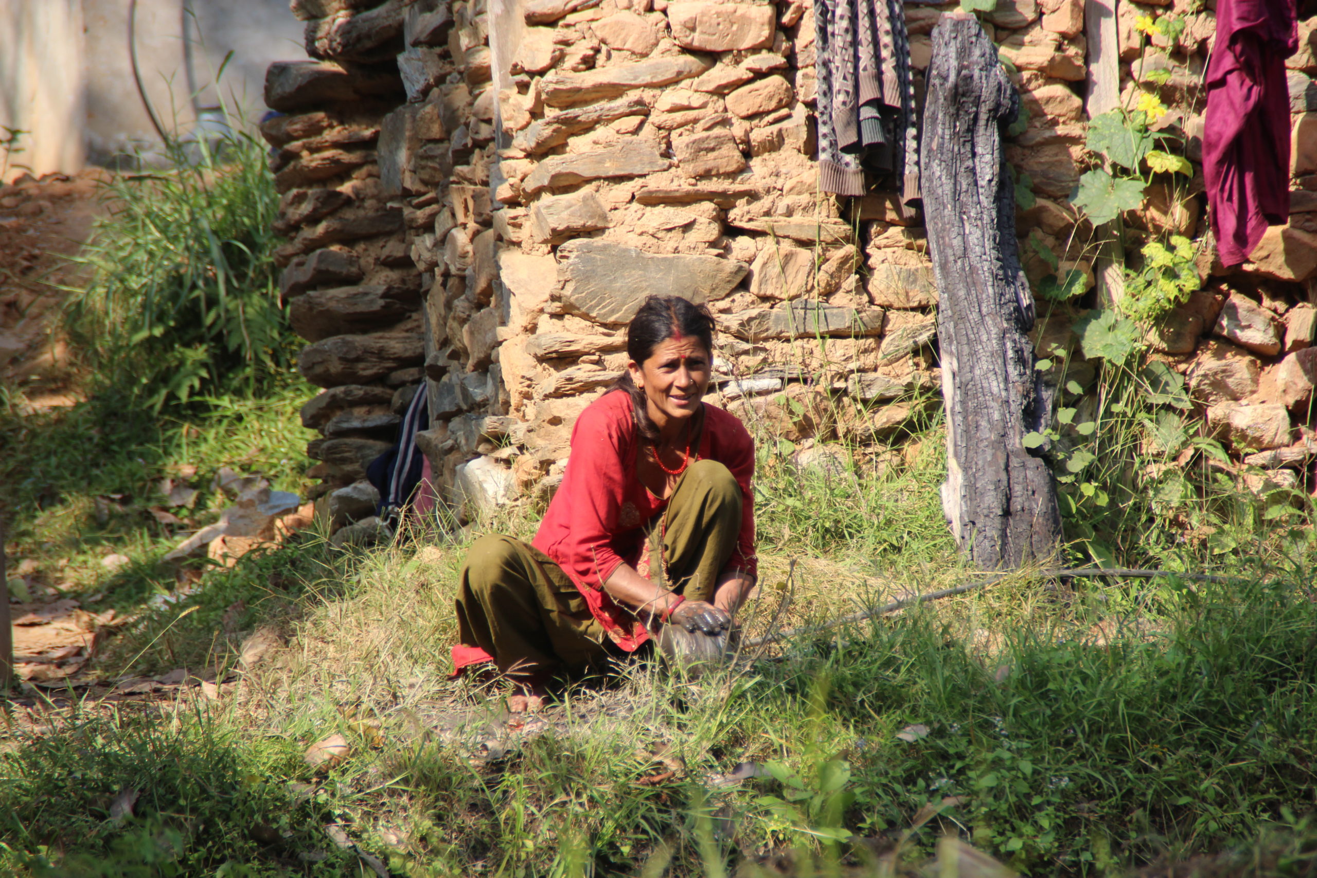 Lady crouching in grass doing washing.